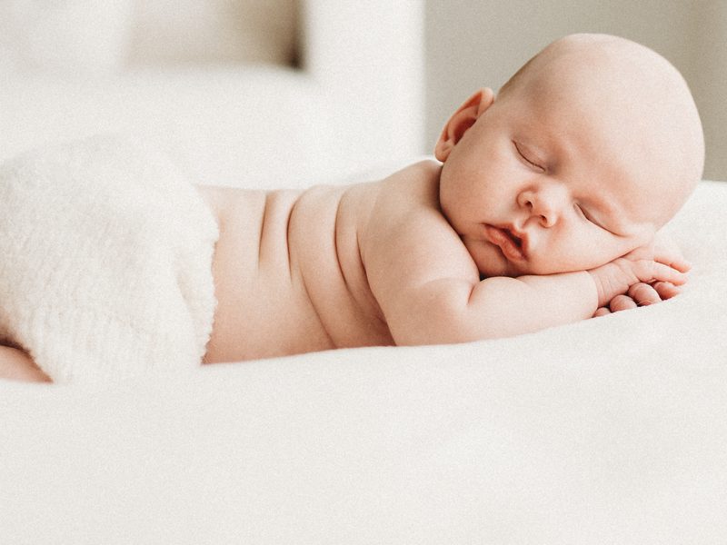 A newborn sleeping on a white bed in a bright room