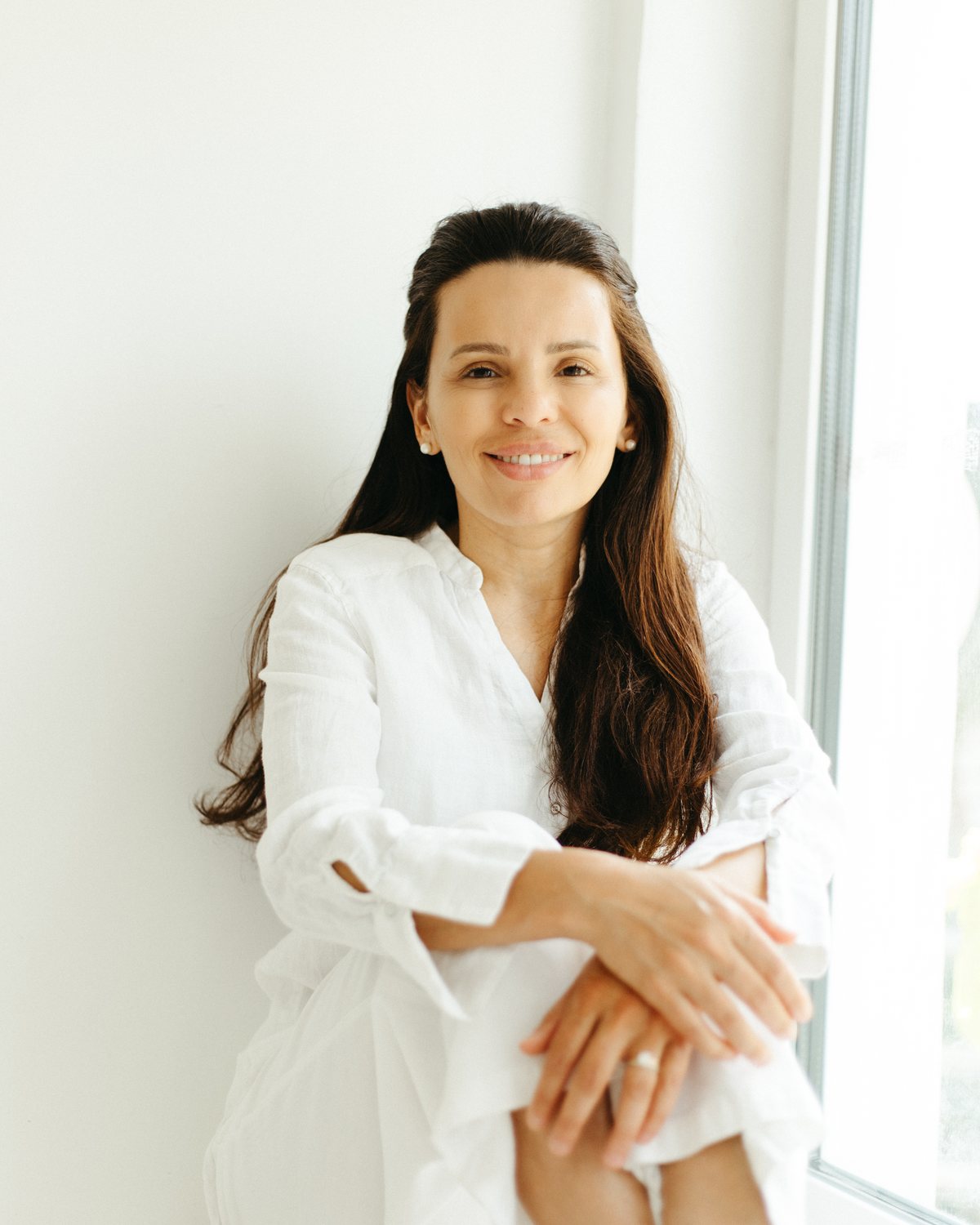Vânia Oliveira-Breen seated beside a bright window, smiling